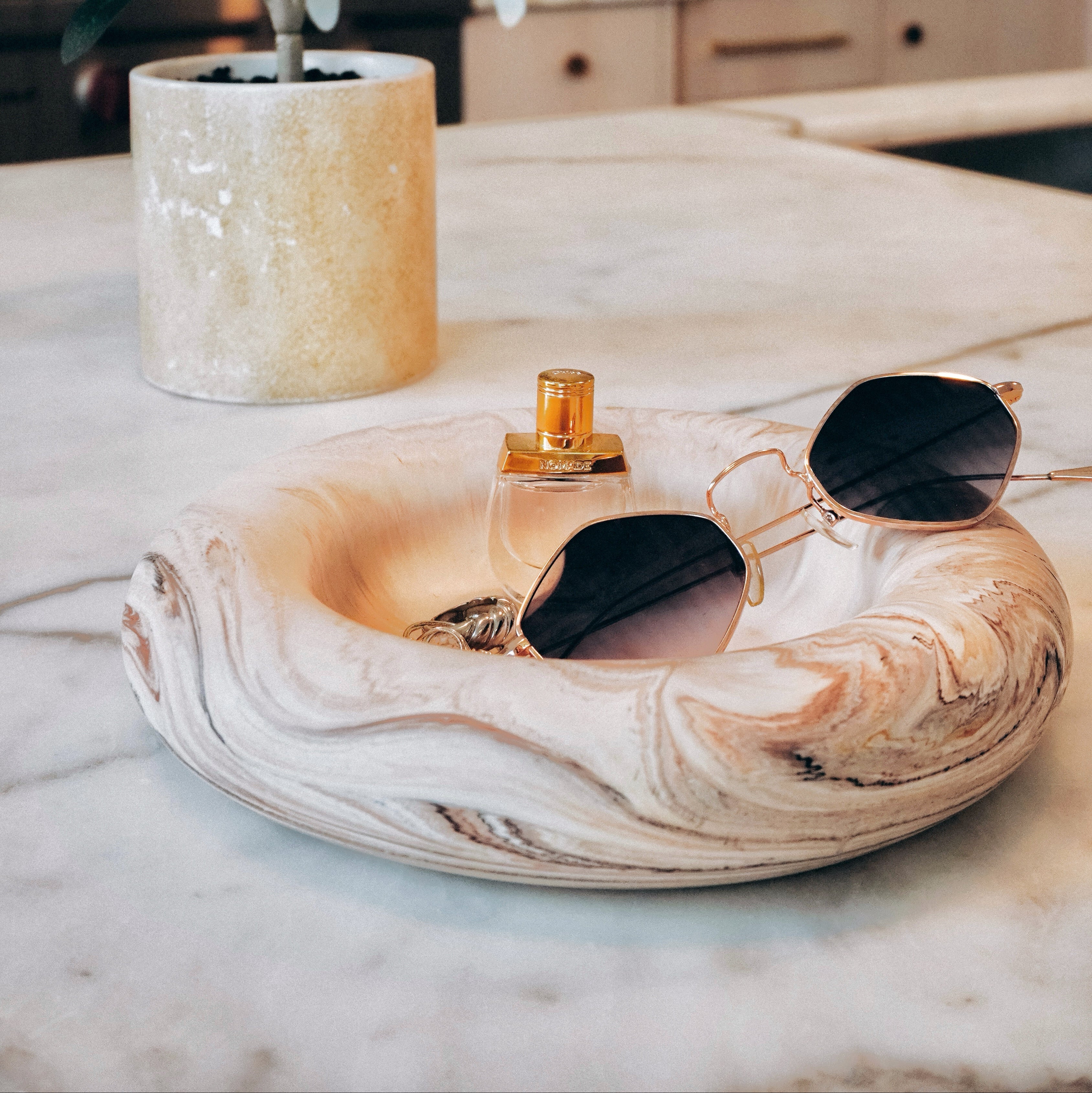 Decorative tray with sunglasses, perfume bottle, and plant on a marble surface.